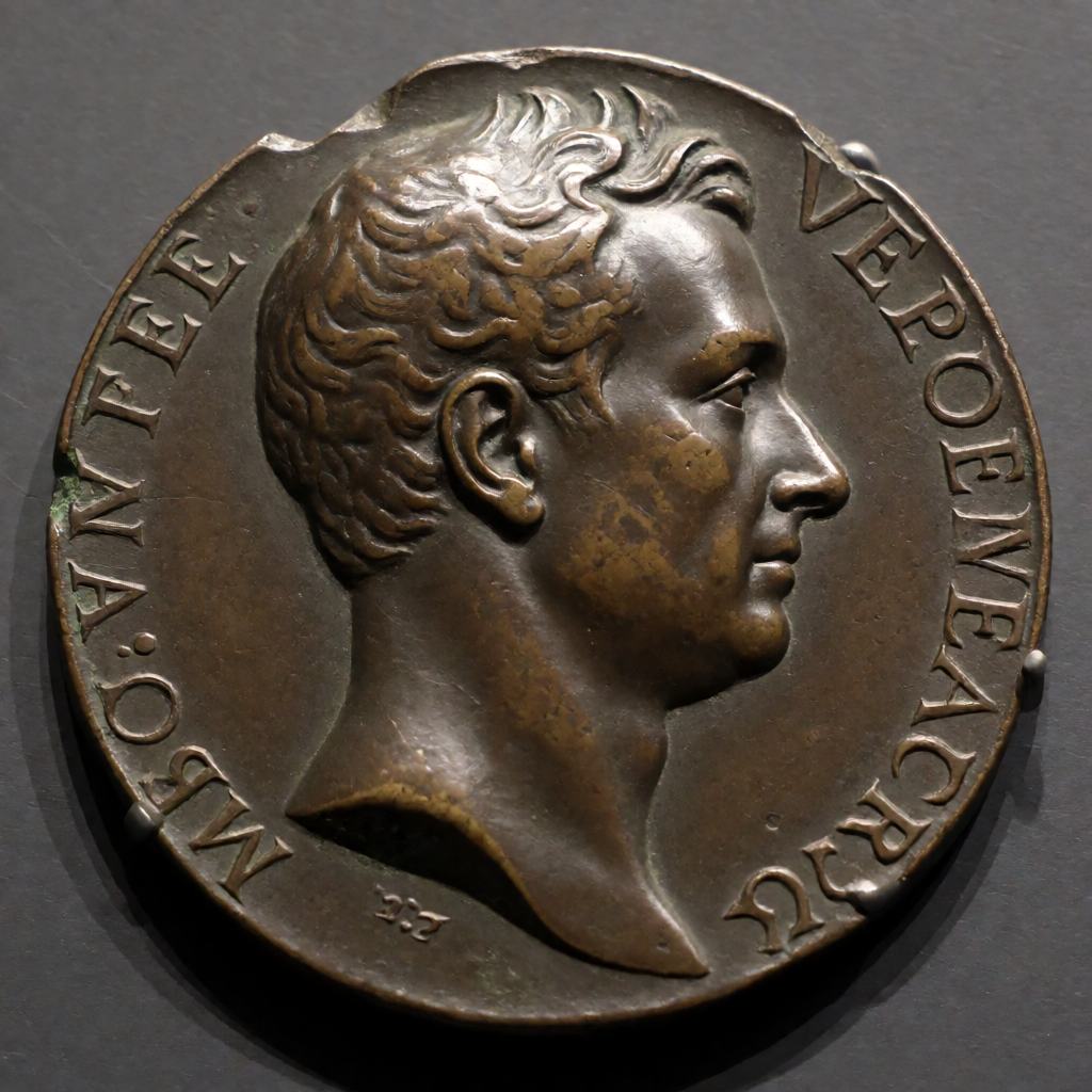 Close-up of a bronze medal struck with a raised profile head and cut lettering round the edge, worn and darkly patinated